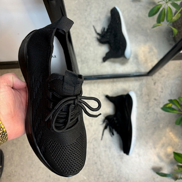Sorte strikkede slip on sko med en fast kant i åbningen.